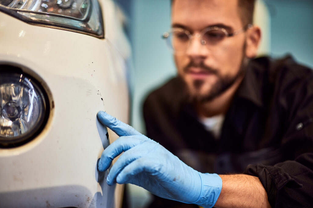 A professional panel beater inspecting visible car damage with a customer beside the vehicle in a clean workshop environment.